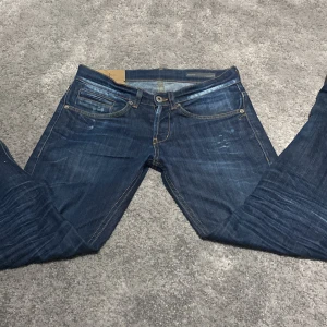 Mörkblå jeans från Dondup - Snygga mörkblå jeans från Dondup med klassisk femficksdesign och kontrastsömmar. De har en knappgylf och är perfekta för en avslappnad stil. Har en pytteliten lilafläck på låret som knappt syns även när man stirrar på den. Står storlek 29 men tycker själv den passar 27 eller 28, längden är 30 