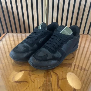 Svarta sneakers från Valentino - Snygga svarta sneakers från Valentino med ett diskret camouflage-mönster. Skorna har snörning och en robust sula för extra komfort. Perfekta för en stilren look.