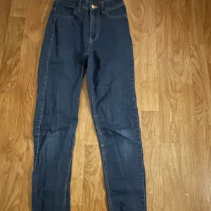 Mörkblå jeansbyxor - Snygga mörkblå jeansbyxor med hög midja och klassisk femficksdesign. Byxorna har en knapp och dragkedja framtill. Perfekta för en stilren look.