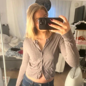 Brun croppad kofta - Säljer en stilren brun croppad kofta med knappar framtill. Perfekt för lager-på-lager och ger en avslappnad look. Passar bra till jeans eller kjol.