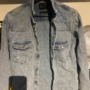 Blå jeansjacka från Zara - Säljer en snygg blå jeansjacka från Zara med avslappnad passform. Skjortan har långa ärmar och två bröstfickor med knappar. Perfekt för en casual look!