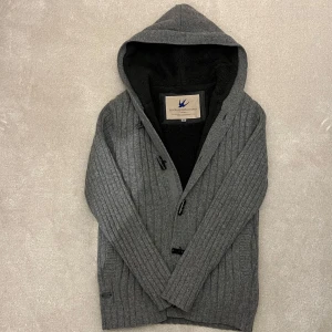 Fodrad Cardigan  - Säljer en snygg grå fodrad cardigan. Den har en mysig huva och knäppning framtill. Perfekt för kyliga dagar med sin mjuka insida och den är i ull vilken gör den extra varm! Vid minsta fråga eller fundering hör av er🤝