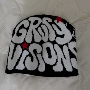 Svart/vit y2k mössa "grvty visions"  - Cool svart mössa med texten 'GRVTY VISIONS' i vitt och röda stjärnor. Baksidan har ett spindelnätsmönster i vitt. Perfekt för en unik stil.