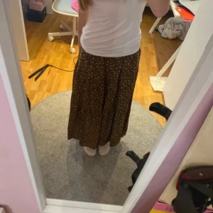 Brun långkjol med blommigt mönster - Säljer en fin brun långkjol med ett litet blommigt mönster. Kjolen har en luftig passform och är perfekt för en avslappnad stil. Den är lätt att matcha med olika toppar och accessoarer.