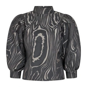 Svart och grå blus med puffärmar - Snygg blus i svart och grått med ett unikt mönster som påminner om träådring. Blusen har puffiga långa ärmar och en hög krage som ger en elegant look. Perfekt för att sticka ut med stil.