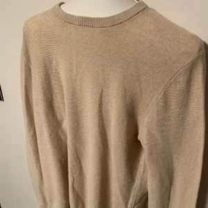 Beige tröja från East West - Säljer en stilren beige tröja från East West. Tröjan har en klassisk rund hals och långa ärmar. Perfekt för en minimalistisk look. Passar bra till både jeans och chinos. Storlek M.