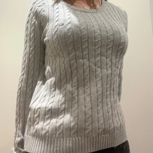 Grå kabelstickad tröja från Lexington - Säljer en stilren grå kabelstickad tröja från Lexington. Tröjan har en klassisk design med rund hals och långa ärmar. Perfekt för kyligare dagar och ger en tidlös look. Lexington-loggan är diskret placerad på bröstet.