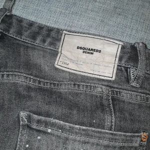 Grå jeans från Dsquared2 - Snygga grå jeans från Dsquared2 med coola slitningar och färgstänk för en unik look. De har en knappgylf och klassisk femficksdesign. Perfekta för dig som vill sticka ut med stil.