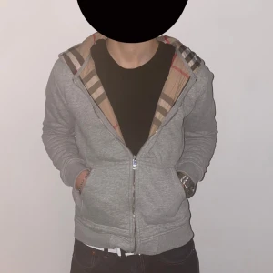 Burberry zip up/hoodie - Säljer en stilren grå zip up/hoodie från Burberry. Produkten är inte använd som ni kan se på bilden ( bara testad ). Om ni vill ha fler bilder eller frågor kontakta via DM. Modellen på bilden är 173 cm och 58kg. 