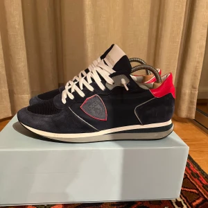 Blå sneakers från Philippe Model - Snygga blå sneakers från Philippe Model med vita snören och röda detaljer. Skorna har en stilren design med mocka och syntetmaterial. Perfekta för en trendig look. Skorna är nästintill nya, knappt använda. Kvitto finns. Skriv i dm om du vill ha mer info kring skorna! Priset kan såklart diskuteras!