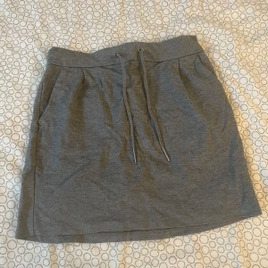 Grå kjol från Vero Moda - Snygg grå kjol från Vero Moda i en bekväm och avslappnad stil. Kjolen har en elastisk midja med snörning men inte riktiga. Perfekt för en casual look. Ganska gammal men inga synliga deffekter 