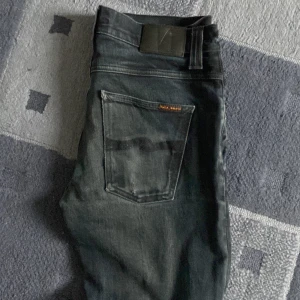 Mörkblå jeans från Nudie Jeans - Snygga mörkblå jeans från Nudie Jeans med klassisk femficksdesign och knappgylf. Jeansen har en subtil tvättad look och märkets logga på bakfickan. Perfekta för en stilren och avslappnad stil. Det är modellen lean Dean och dem är i bra skick. Storleken är 32/34 men skulle säga att de passar 32/32!