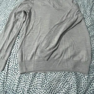 Grå v-ringad tröja - Säljer en stilren grå tröja med v-ringning och långa ärmar. Perfekt för en avslappnad look. Tröjan har ribbade muddar vid ärmslut och nederkant.