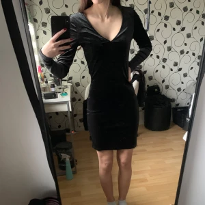 Svart sammet klänning - Snygg svart klänning i sammet med v-ringning och långa ärmar. Perfekt för en elegant look eller för finare tillfällen. Klänningen har en tight passform som framhäver figuren. Har ett ”kallt” tyg på insidan. 