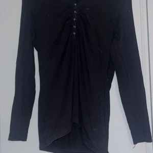 Svart långärmad topp från KappAhl - Säljer en stilren svart långärmad topp från KappAhl med knapprad framtill. Perfekt för en enkel och elegant look. Passar bra till både jeans och kjol. 🖤