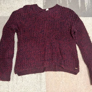 Vinröd stickad tröja - Säljer en mysig vinröd stickad tröja med ett melerat mönster. Tröjan har långa ärmar och ribbstickade muddar vid ärmslut och nederkant. Perfekt för kyliga dagar!