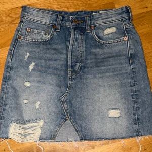 Blå jeanskjol med slitningar - Blå jeanskjol med slitningar och fransig nederkant. Helt oanvänd!