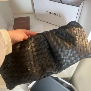 Svart flätad kuvertväska - Snygg svart flätad kuvertväska i skinn. Perfekt för att ge din outfit en stilren touch. Väskan har en elegant design och är lätt att bära med sig.