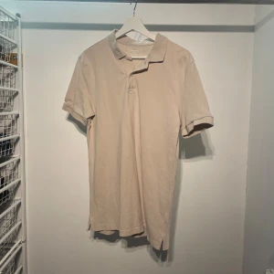 Beige pikétröja - Säljer en stilren beige pikétröja med klassisk krage och korta ärmar. Perfekt för en avslappnad men ändå snygg look. Passar bra till både jeans och chinos.