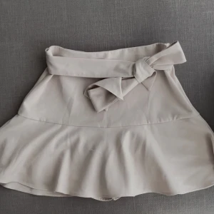 Beige kjol med rosett - Snygg beige kjol med volang och en stor rosett framtill. Kjolen har inbyggda shorts oxå!! Gamla från Zara🫶🏽🫶🏽🫶🏽🫶🏽