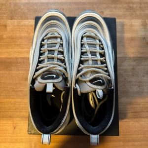 Nike Air Max 97 cool grey - Snygga Nike Air Max 97 sneakers i en stilren grå och silver färgkombination. Skorna har den ikoniska vågformade designen med synlig Air-dämpning i sulan för extra komfort. Perfekta för både stil och funktion. Använda ca 3 gånger.