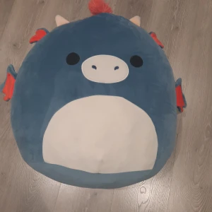 Blå Squishmallow drake - Mysig och stor blå Squishmallow i form av en drake med röda detaljer och en vit mage. Den har en söt design med små horn och en röd man längs ryggen. Perfekt för lek eller  dekoration i rummet. hälst kommas och hämtas❤️ tryck inte köp nu!