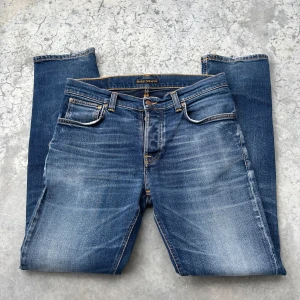 Nudie jeans  - Nudie jeans Grim Tim i färgen Navy. Snygga slitningar i storlek 33/32, dock en liten defekt vid bakfickan 