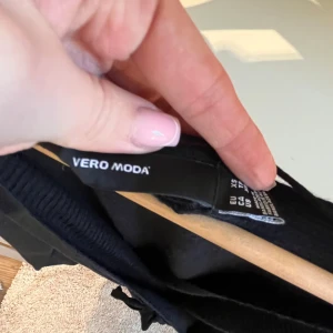 Svart omlottkofta från Vero Moda - Säljer en stilren svart omlottkofta från Vero Moda. Koftan har långa ärmar och ett knytband i midjan för en justerbar passform. Perfekt för lager-på-lager-stil och att hålla sig varm under kyliga dagar.