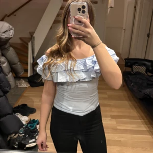 Ljusblå offshoulder topp med volanger - Säljer en söt ljusblå offshoulder topp med volanger. Perfekt för en somrig look. Toppen har en tight passform och är tillverkad i ett mjukt material.