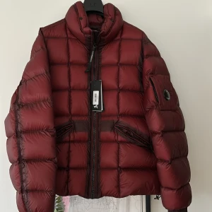 Vinröd dunjacka från C.P. Company - Säljer en snygg vinröd dunjacka från C.P. Company. Jackan har en quiltad design med dragkedja framtill och en cool detalj på ärmen. Perfekt för kyliga dagar. Men känns lite tunnare så vinter/vår, helt ny tag kvar kvitto finns! 52, men sitter som M