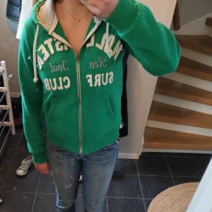 Zip up hoodie - Grön zip up hoodie från Hollister. Grå i luvan och vita snören. Passar storlek S-M 