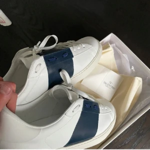 Valentino open  - Snygga Valentino Open sneakers i vitt med en bred blå remsa över ovansidan. Skorna har en stilren design med snörning och en bekväm sula. Perfekta för en trendig look. Bilderna är lite gammla och har använt de lite , vid mer bilder så är det bara att skriva . Kan gå ner i pris vid snabb äffär, stolrek 45 men passar perfekt till 44, skorna har ett litet Jack vid sidan men syns inte och går att fixa väldigt lätt 