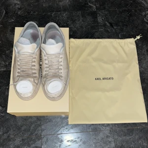 Axel arigato Clean 90 Sneaker White - Snygga vita sneakers från Axel Arigato med klassisk snörning. Skorna har en stilren design och kommer med originalförpackning och påse. Skorna är i bra skick! Inga skavanker, dem ser ut att vara i sämre skick än vad de är pga smutsen! Med en bra skotvätt och de nya snörena som följer med blir dem nog riktigt prisvärd och fräsch! 