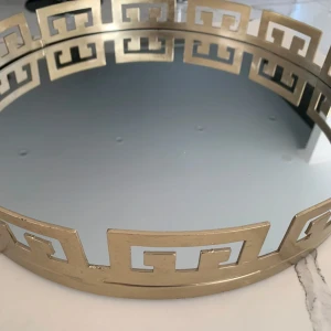 Rund spegelbricka med guldkant - Elegant rund spegelbricka med en dekorativ guldkant i geometriskt mönster. Perfekt som dekoration eller för att arrangera ljus och små föremål. Den spegelblanka ytan reflekterar ljus vackert och ger en lyxig känsla till rummet.