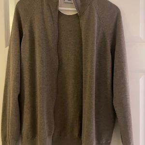 Beige full zip från MNG - Säljer en stilren beige full zip från MNG med dragkedja. Tröjan har långa ärmar och en ribbad krage. Perfekt för en avslappnad look. Varan har inga tecken på användning.