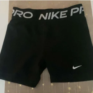 Svarta träningsshorts från Nike - Snygga svarta träningsshorts från Nike med elastisk midja och vit logga. Perfekta för gymmet eller löprundan. Bekväma och stilrena med en tight passform.