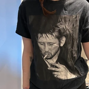 Svart t-shirt med tryck - Svart t-shirt med ett stort tryck av artisten Shane MacGowan. Perfekt för en avslappnad stil. Storlek M :)