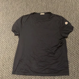 Svart t-shirt från Moncler - Snygg mörkblå t-shirt från Moncler med rund hals och korta ärmar. Den har en broderad Moncler-logga på ärmen. Perfekt för en stilren look. T-shirten är i princip i nyskick och självklart äkta vilket kan bevisas på gr koden. Loggan på armen kan även skannas via MFF-tag Nypris ca 3500 kr. Mitt pris 1250kr! Skriv vid funderingar💭🤩