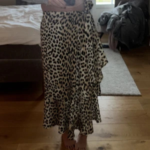 Leopardmönstrad kjol från Gina Tricot - Snygg leopardmönstrad kjol från Gina Tricot i omlottmodell. Kjolen har en knytning i midjan och är perfekt för att ge en trendig look. Den är i en längre modell och passar utmärkt för olika tillfällen.