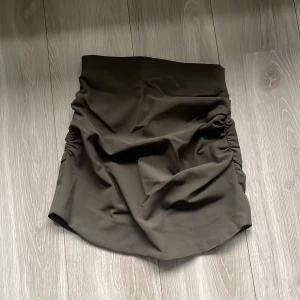Olivgrön kjol från Zara - Snygg olivgrön kjol från Zara i storlek S. Kjolen har en tight passform med rynkade detaljer på sidorna som ger en cool look. Perfekt för höst och vår, och funkar både till vardags och fest. Dragkedja baktill.