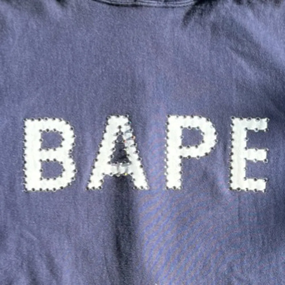 Säljer en snygg blå hoodie från BAPE i 100% bomull. Den har en stor BAPE-logga på framsidan med kristaller runt och en liten logga på baksidan. Perfekt för både höst och vår, med en skön passform och klassisk stil. Bra skick, storlek S. . Tröjor & Koftor.