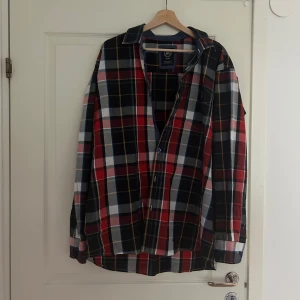 Rutig skjorta i rött, blått och vitt - Säljer en rutig skjorta i rött, blått och vitt. Skjortan har långa ärmar och knappar framtill. 