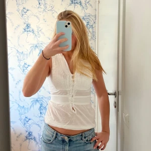 Vit ärmlös blus - Säljer en söt vit blus med knappar framtill och ribbade detaljer. Käpt second hand men aldrig använd då den är lite för liten på mig! 