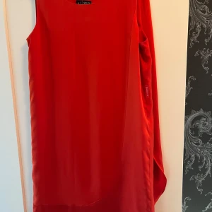 Röd klänning från Armani Jeans - Snygg röd klänning från Armani Jeans i ett elegant och stilrent snitt. Perfekt för festliga tillfällen. Klänningen är ärmlös och har en mjuk, glansig finish som ger en lyxig känsla. Passar perfekt för både sommar och nyårsfester. Strl 42 i klänningen men mer storlek 40 (M). 