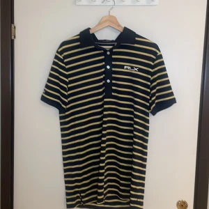 Randig pikétröja från Ralph Lauren - Säljer en snygg randig pikétröja från Ralph Lauren i svart och gul. Tröjan har korta ärmar och en klassisk krage med knappar. Perfekt för en avslappnad men stilren look. Passar både till vardags och festliga tillfällen. 🖤💛priset kan alltid förhandlas!