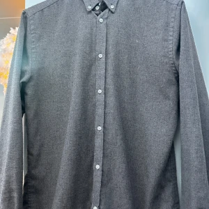 Grå/brun skjorta från Les Deux - Säljer en stilren grå/brun skjorta från Les Deux i storlek M. Skjortan har långa ärmar och knappar framtill. Den är broderad med 'II' på bröstet vilket ger en snygg detalj. Perfekt för både vardag och fest!