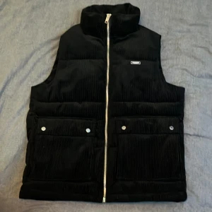 Svart manchesterväst från Jack & Jones - Säljer en snygg svart manchesterväst från Jack & Jones i storlek M. Knappt använd, passade inte mig. Alltså i helt nytt skick. Västen har en dragkedja framtill och två fickor med knappar. Perfekt för höst och vår när du vill hålla stilen utan att frysa. Passar både till vardags och lite finare tillfällen.