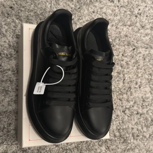 Alexander McQueen skor  - Svarta Alexander McQueen skor. Med guldig text. Väldigt stiliga och perfekta skor för bröllop, fester eller bara gå runt me i stan. Jätte sköna skor också och helt nya och uanvända. Kommer med originala boxen och påsen. Priset kan diskuteras. 