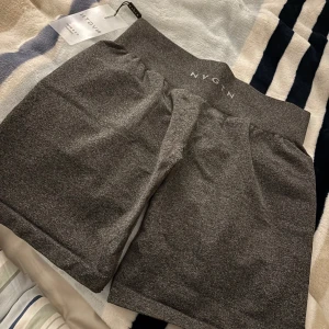 Grå shorts från NVGTN - Säljer ett par grå shorts från NVGTN i mycket bra skick. De är midwaist och har en tight passform, perfekta för träning. Materialet är mjukt och stretchigt, vilket gör dem bekväma att bära. Perfekta för gymmet eller en aktiv dag!