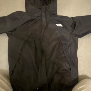 Svart vindjacka från The North Face - Säljer en svart vindjacka från The North Face i mycket bra skick. Jackan har en huva och dragkedja framtill, perfekt för blåsiga dagar. Den är stilren och passar till det mesta. Perfekt för höst och vår!